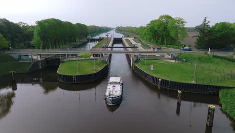 aerial zoom out from a barge leaving doerpen lock on the küstenkanal, showing symmetrical canal design and surrounding greenery under clear skies.