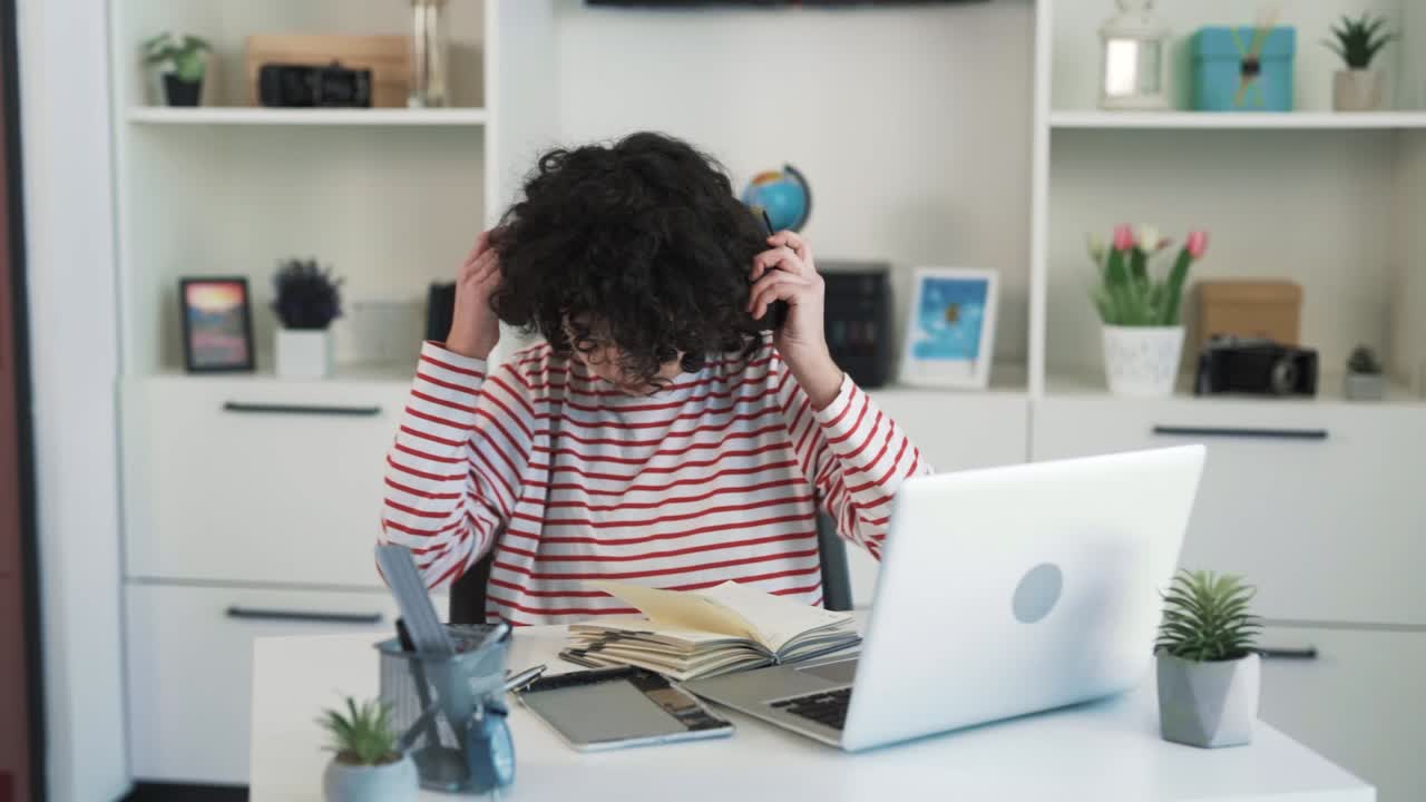 una chica con el pelo rizado y una cara atractiva está escuchando música con auriculares inalámbricos mientras se sienta en un escritorio en una oficina luminosa y disfruta de la canción