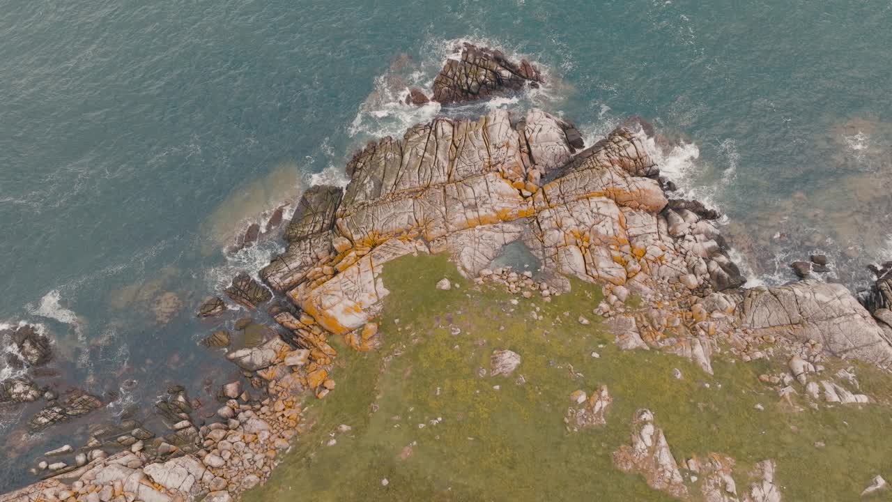 Ondas quebrando em falésias com grama verde e água azul
