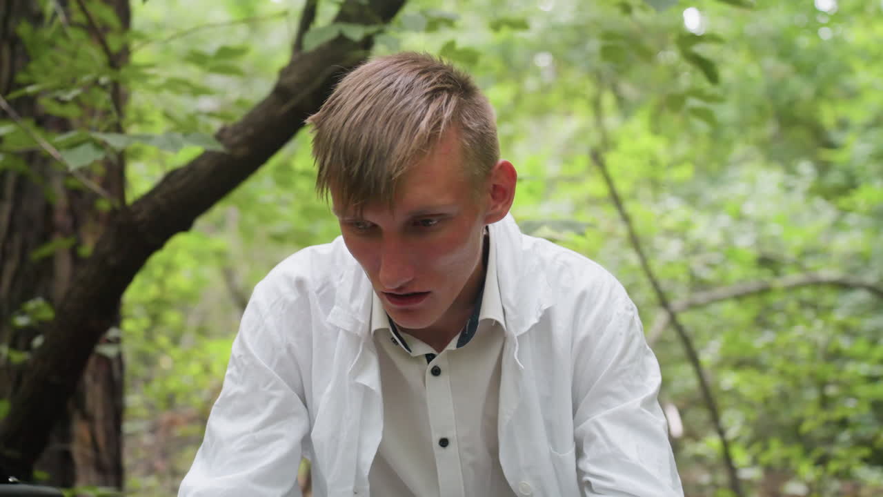 Botany student in white coat and glasses resting in forest with tired expression, reflecting fatigue during outdoor work and showing visible stress while sitting among trees during field study
