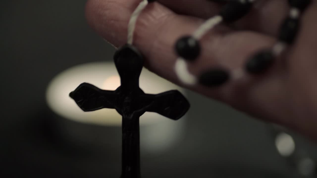 Fingers holding string of rosary beads close up with candle background