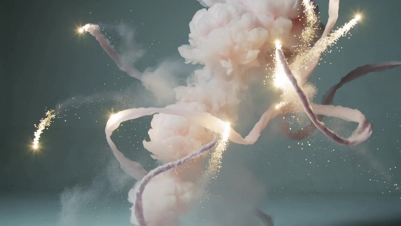 Una colonna di fumo rosa si alza, partendo da un'accensione a terra in studio, formando anelli con nastri e scintille.