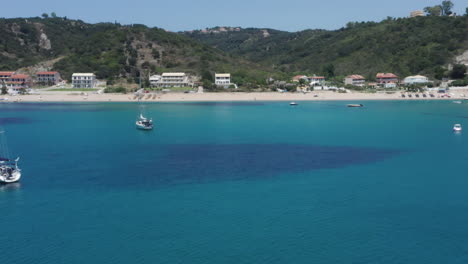 Aerial-shot-approaching-a-Mediterranean-sandy-beach-below-the-forest-covered-mountains