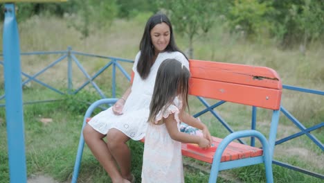 a pregnant mother and her young daughter enjoy playful time together at a playground in the park, surrounded by trees and greenery