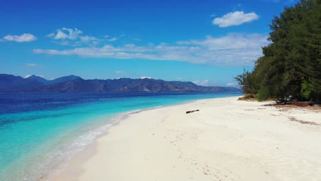 Scenic-view-of-shallow-aqua-waves-crashing-against-the-white-sand-with-beautiful-mountains-in-the-distance