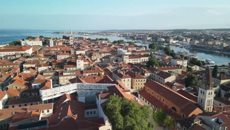 An-aerial-over-old-town-Zadar-with-red-rooftops,-church-towers-and-distant-bridge-and-the-rest-of-the-city