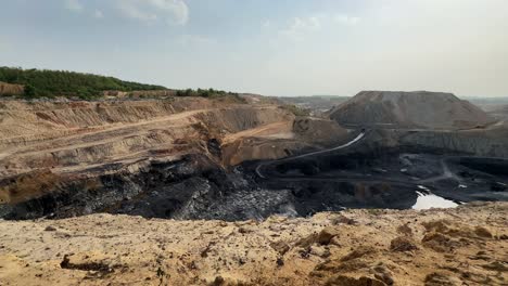 a wide sweeping panning shot reveals the sheer scale of an open-pit coal mine in india