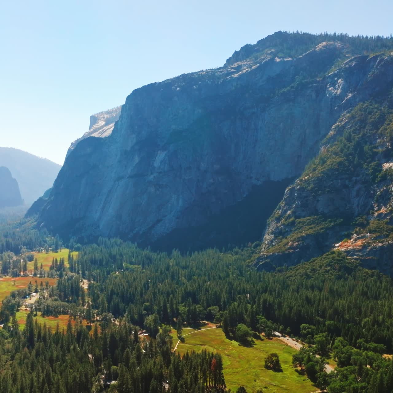 Flying over the picturesque green valley covered with pine tree woods. Sunny scenery of rocks in Yosemite National Park, USA. Top view