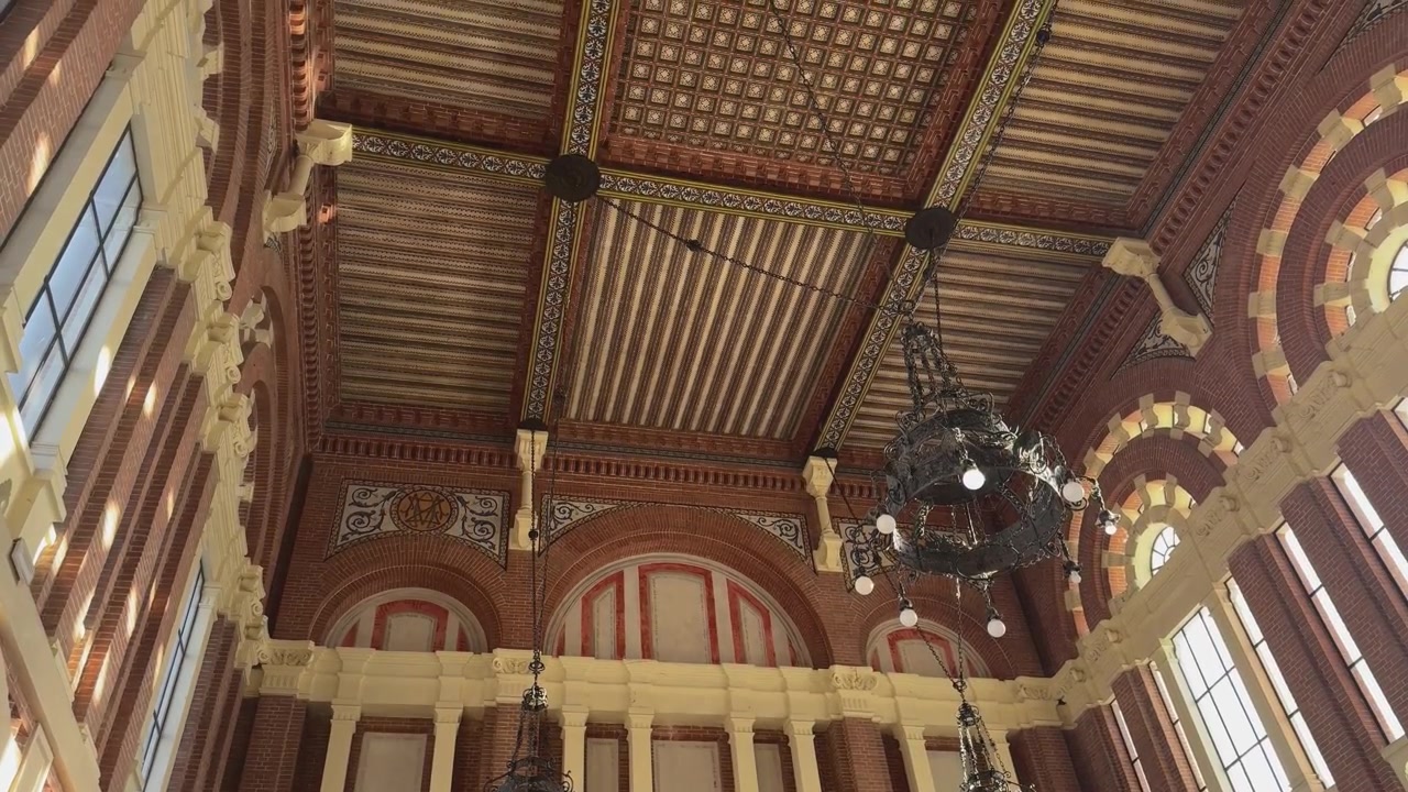 Mouvement de caméra ascendant à main levée à l'intérieur du hall principal de la gare d'Aranjuez, révélant trois murs avec des détails néo-mudéjars avant de se terminer sur le plafond ornemental richement décoré