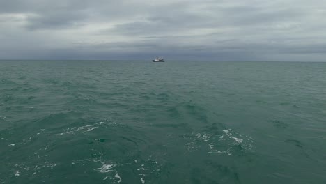 A-fishing-boat-on-the-horizon-gets-hidden-behind-a-big-swell-in-the-ocean