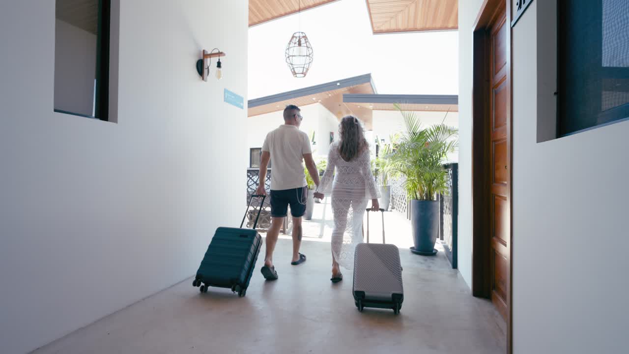Couple Walking with Luggage Through a Modern Resort Hallway