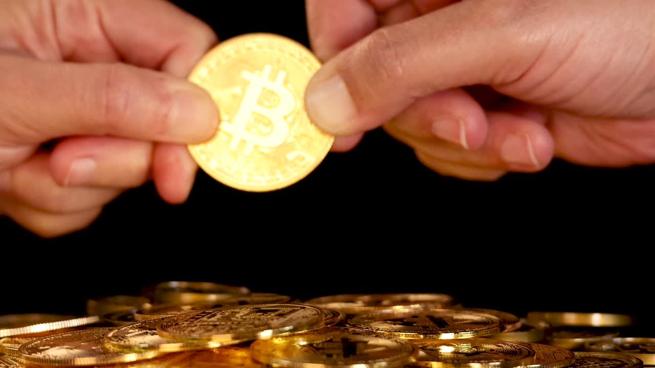 Two hands pull a gold digital coin above a pile, dramatic lighting, close-up, black background