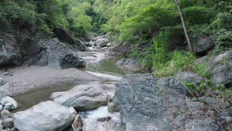 Drone-flight-over-tranquil-rocky-stream-in-tropical-area-of-Dominican-Republic-at-daytime