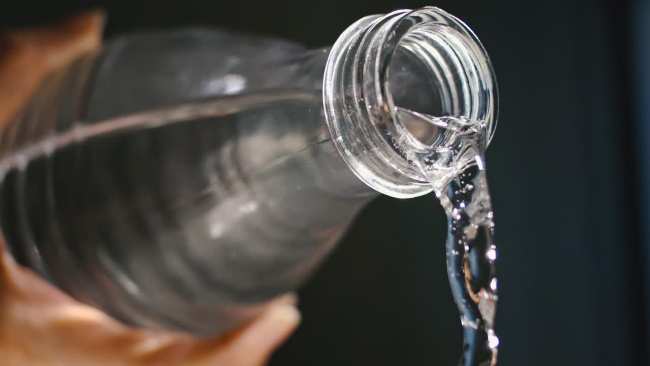 mano masculina vertiendo una maravillosa corriente de agua de una botella de vidrio, mantenerse saludable, hidratarse, en cámara lenta, a alta velocidad