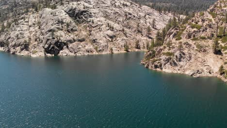 fast aerial shot of pine trees and granite on the shore of a high sierra lake in california