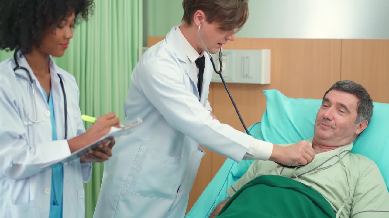 Doctor and assistance nurse visit patient in the room and using stethoscope checking up heart beat rate. Older man lying on the bed and breathe in and breathe out during doctor listening.