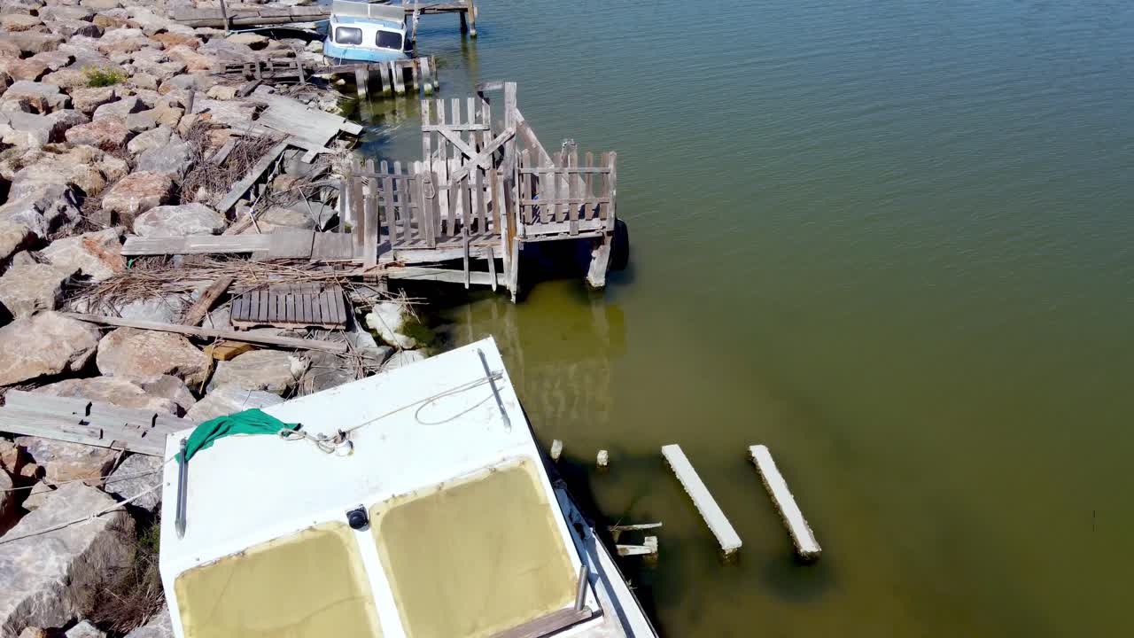Small motorboats and old fishing vessels along a rocky river shoreline as seen from a drone flying at low altitude