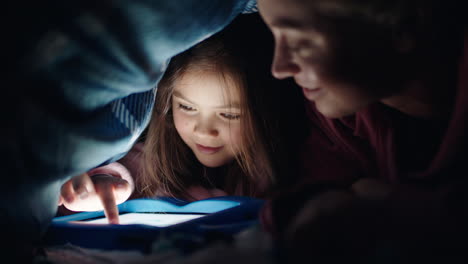 Glückliche-Mutter-Und-Tochter,-Die-Unter-Der-Decke-Einen-Tablet-Computer-Benutzen-Und-Spiele-Auf-Touchscreen-Technologie-Spielen,-Sich-Entspannen-Und-Vor-Dem-Schlafengehen-Spaß-Haben