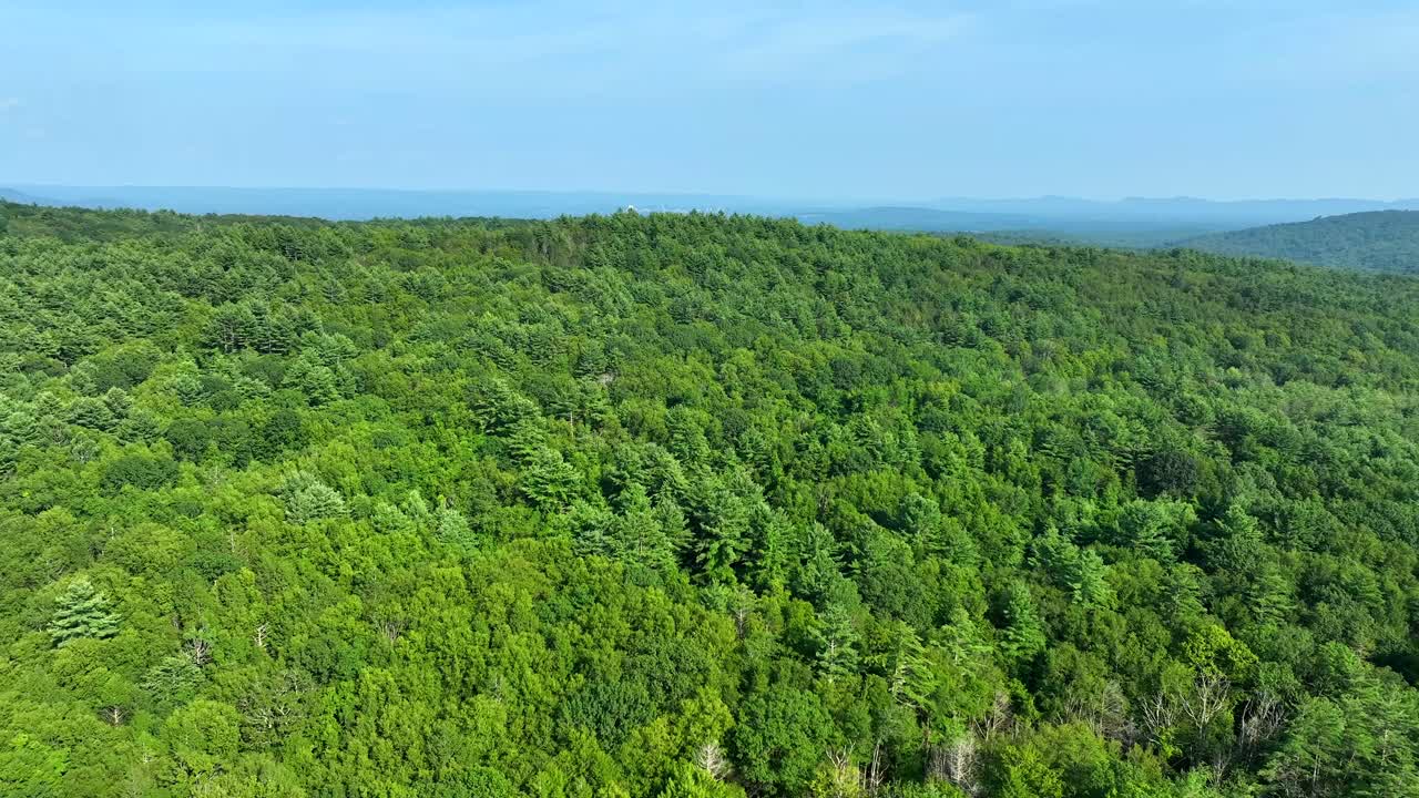 Aerial view over lush forested hills in New England under blue summer sky