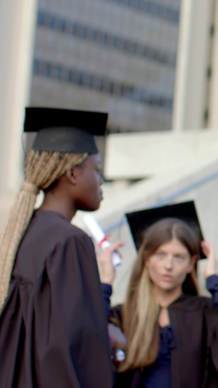 Vertikal video: To dimittender i kåber går ind og vender sig mod en klassekammerat på pladsen, der retter på huer