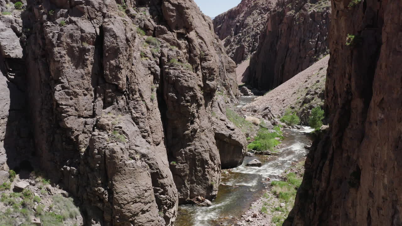 un dron captura una vista impresionante de los altos acantilados que rodean un desfiladero de río sereno, bañado en el resplandor de la luz del sol del mediodía