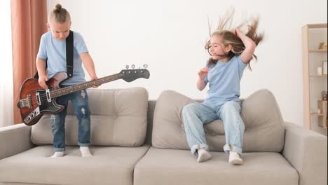 little boy playing electric guitar, children having fun at home on the couch. brother and sister are having fun and dancing in the living room