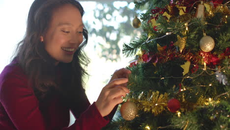 Happy-biracial-woman-decorating-christmas-tree-and-smiling,-slow-motion