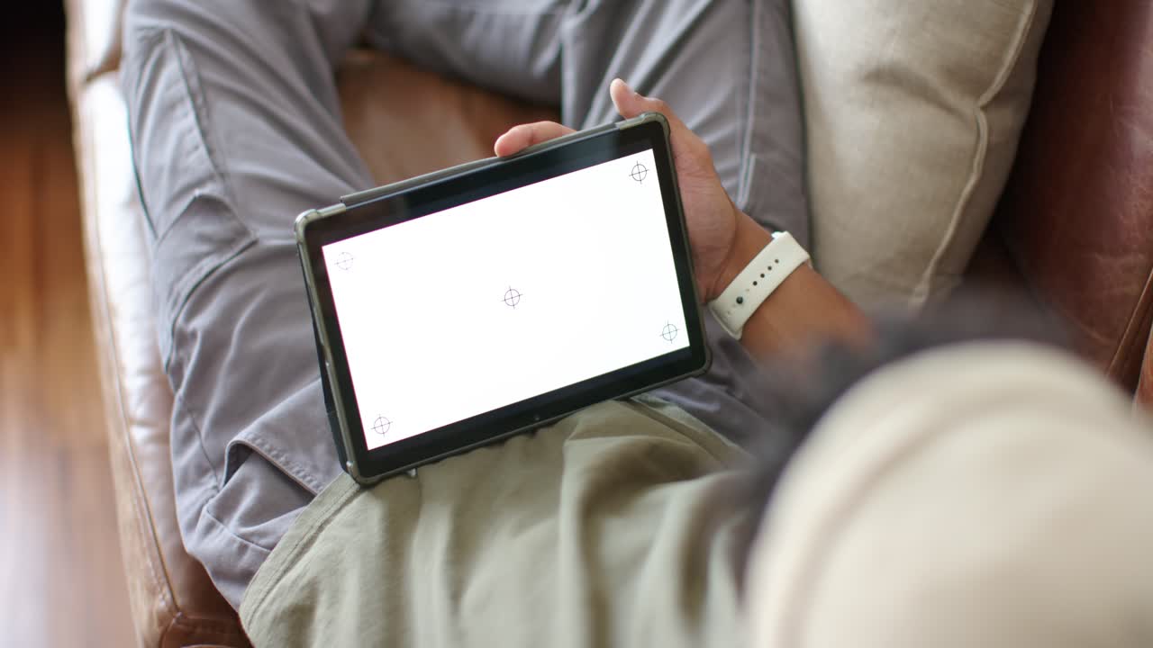 Man is reclining on sofa, tablet resting on lap while adjusting tilt to align markers