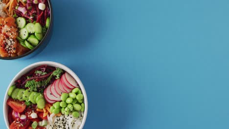 Composition-of-bowls-with-rice,-salmon-and-vegetables-on-blue-background