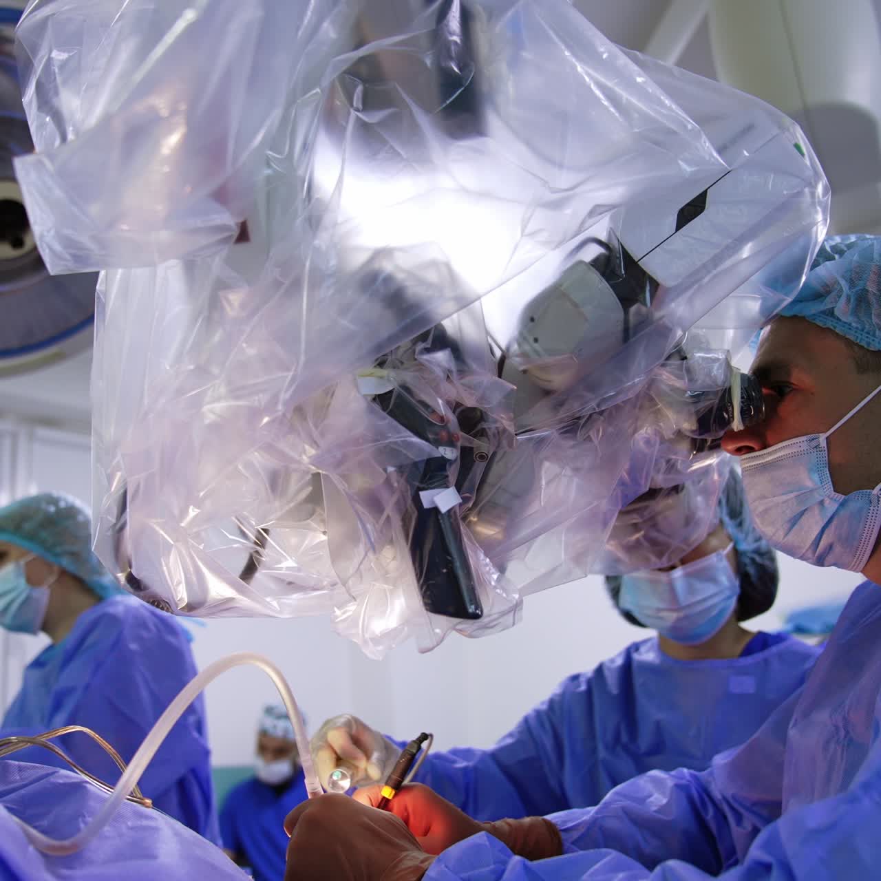 Male surgeon looks at microscope covered with plastic. Focused neurosurgeon uses modern surgical tools at operation. Low angle view