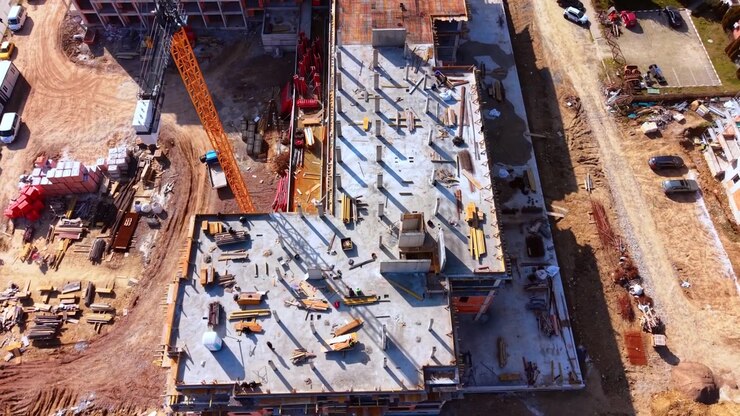Elevated view of concrete rooftop construction site. Building materials, timber and a crane surround an unfinished slab seen from above.