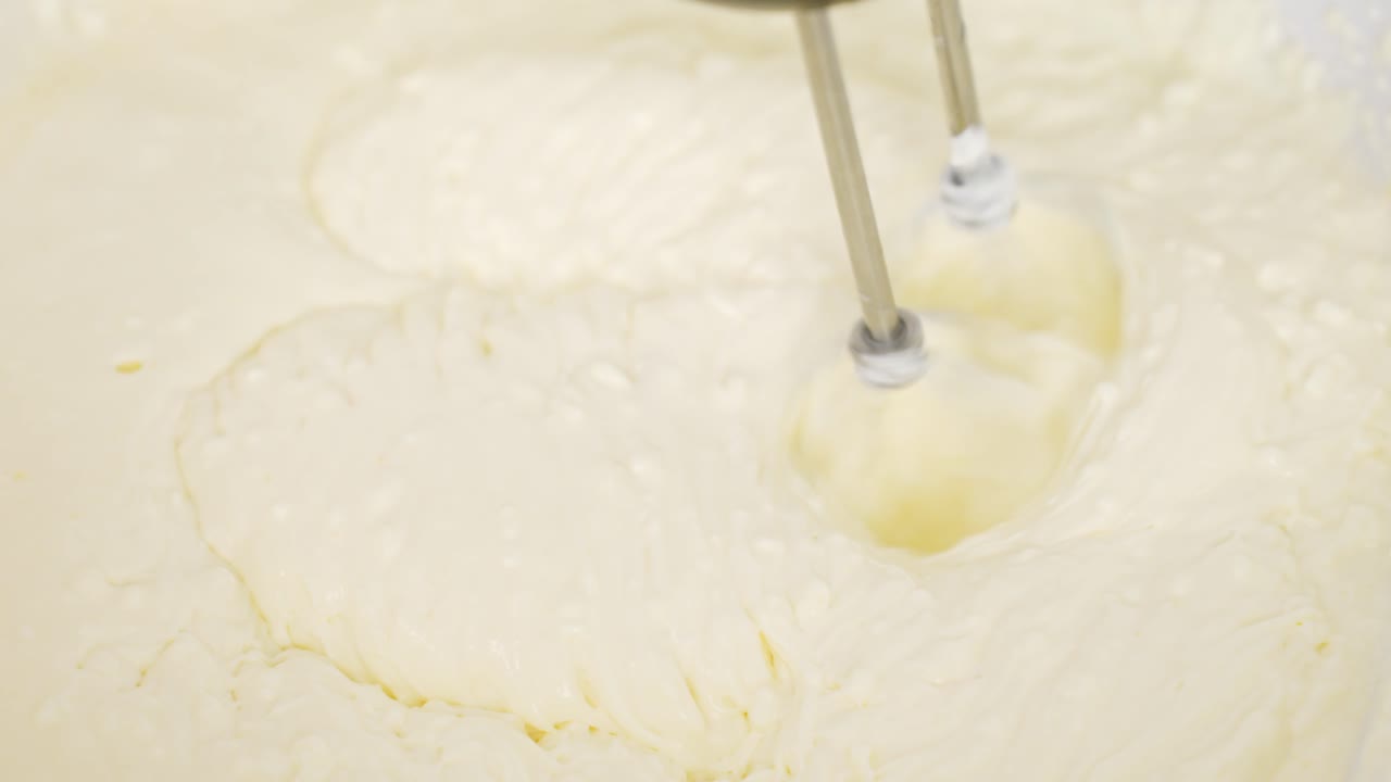 Top-down close-up shows electric beaters mixing mascarpone, egg yolk and powdered sugar into fluffy tiramisu cream, visible motion swirls and rich texture, real time, static shot