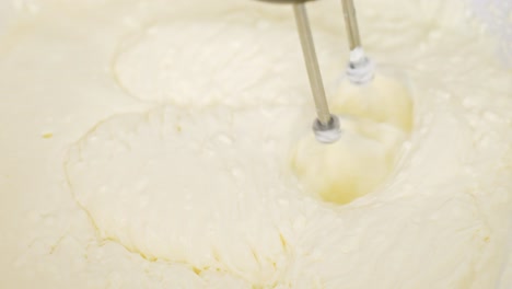 top-down close-up shows electric beaters mixing mascarpone, egg yolk and powdered sugar into fluffy tiramisu cream, visible motion swirls and rich texture, real time, static shot
