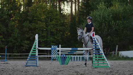 Young-female-rider-on-bay-horse-jumping-over-hurdle-on-equestrian-sport-competition