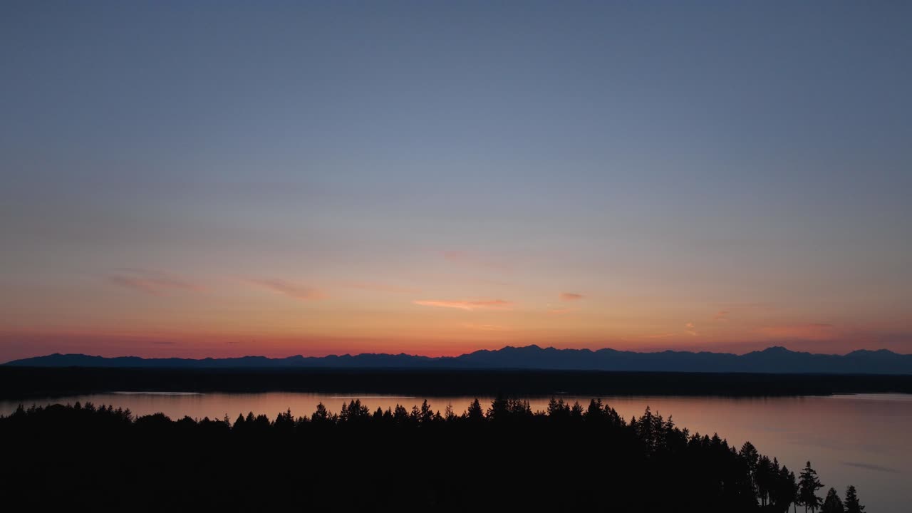 Drone shot of Herron Island's trees silhouetted in the setting sun's glow in Washington State