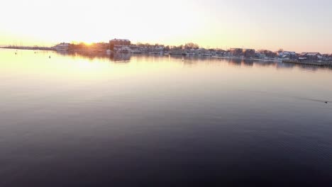 Muelle-Cubierto-De-Nieve-Toma-Aérea-Muy-Baja-Sobre-Pilotes-Y-Sobre-El-Río-Durante-La-Salida-Del-Sol-Dorado-En-La-Histórica-Annapolis,-Maryland