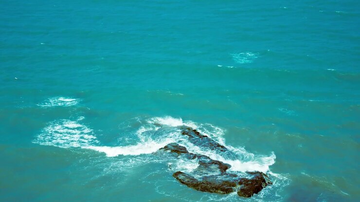 Video panoramico dall'alto di onde del mare turchese che si infrangono contro una roccia parzialmente sommersa con schiuma bianca, con un aspetto da pellicola vintage nostalgica e caldi colori retrò in una giornata di sole.