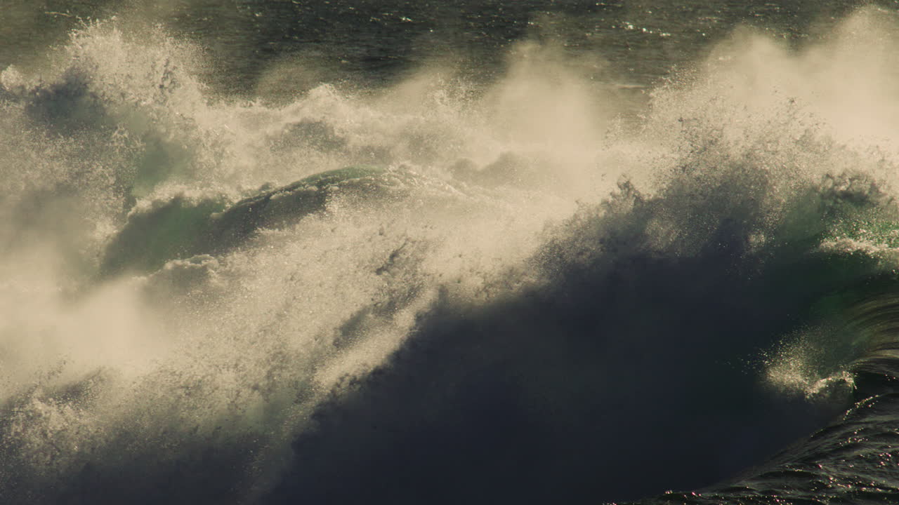 Stormy sea spray rises with large wave, thick mist and curling foam in high contrast dusk