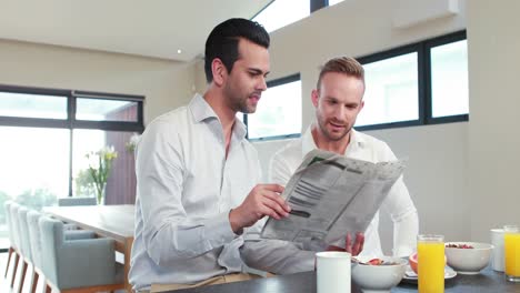 homosexual couple reading newspaper in the kitchen