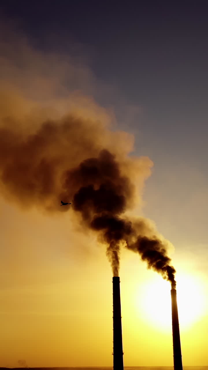 Two industrial pipes with dark smoke at sunset. Massive dense of toxic emissions from industrial factory filling the sky in the evening. Polluting the atmosphere. Vertical video