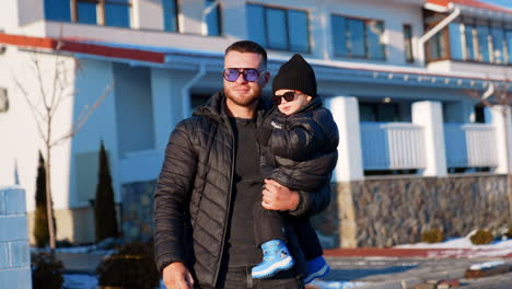 proud father holding his little son standing outdoors in winter. cute baby boy wearing sunglasses points ahead.