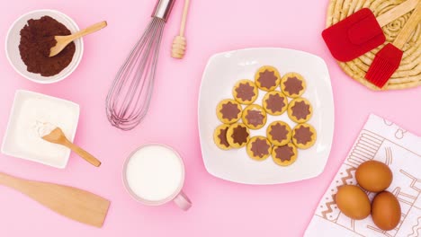 eggs, milk, cacao,flour, cookies in plate and items for baking appear on pink theme. stop motion