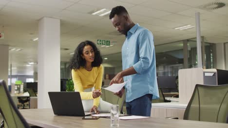 video of happy diverse businessman and businesswoman using laptop, talking about project