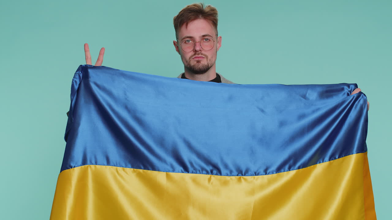 Man holding ukraine national flag showing victory sign against war hoping for success and win