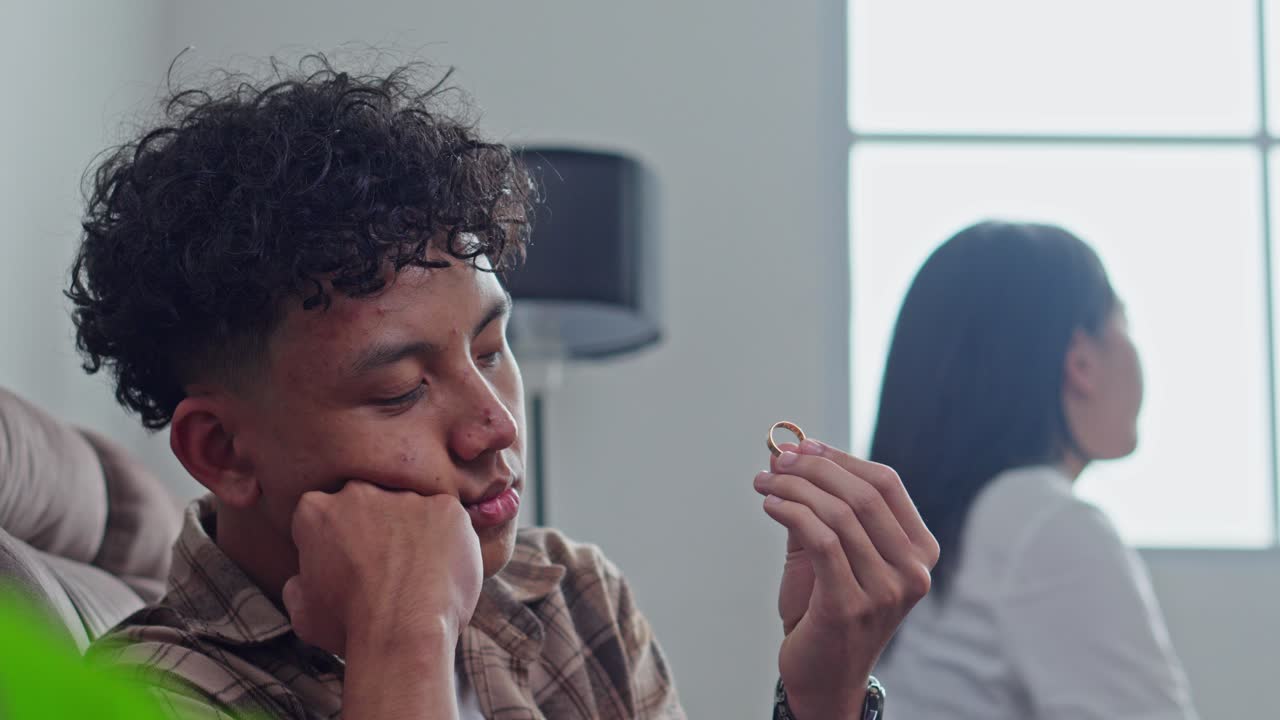 Jovem marido triste olhando para a aliança após discussão com a esposa.