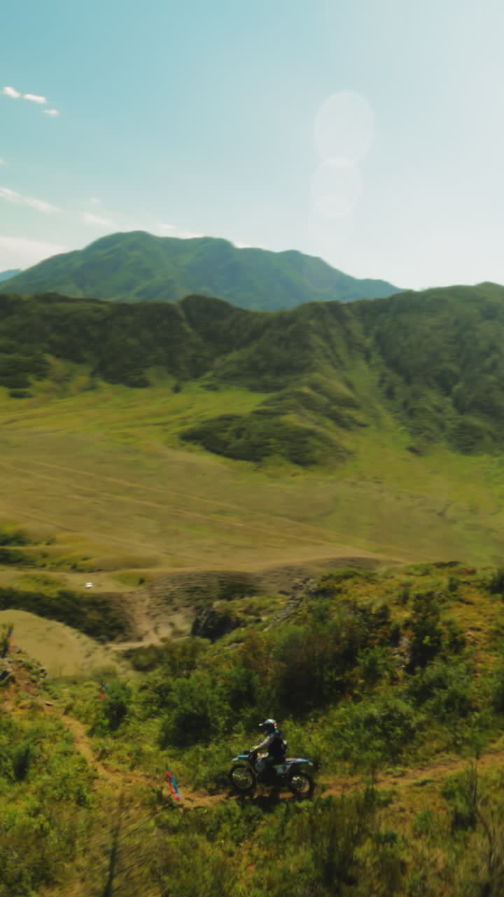 Motorcyclist rides vehicle slowly along ridge fpv. Sportsman in protective helmet rides motorbike along ground road on wooded mountain. Extreme racing