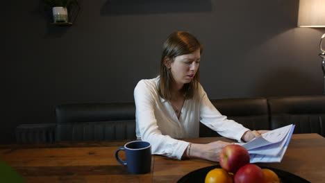 A-stressed-young-brunette-woman-with-head-in-hands-and-bills-and-a-letter-on-the-table-as-she-is-worried-and-depressed-in-the-kitchen-at-home