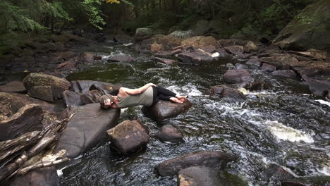 female figure resting on rocks at the river