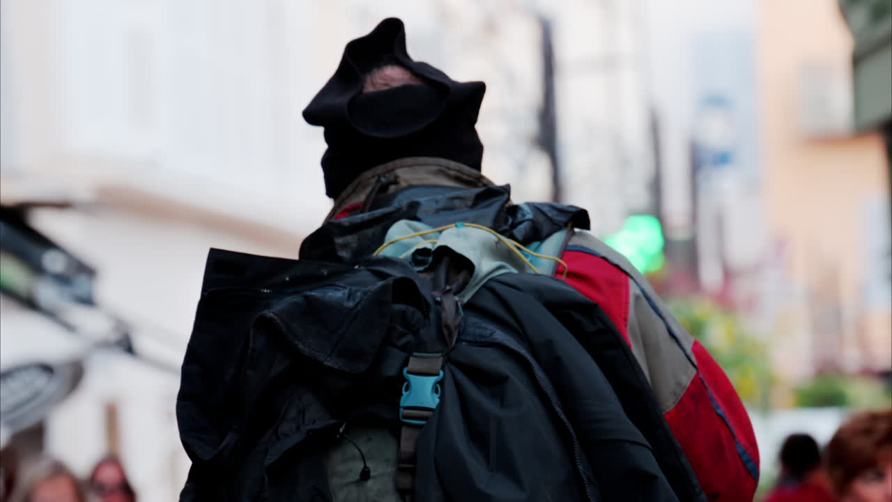 Close up of a man with multiple dirty clothes on his backpack moving through the city