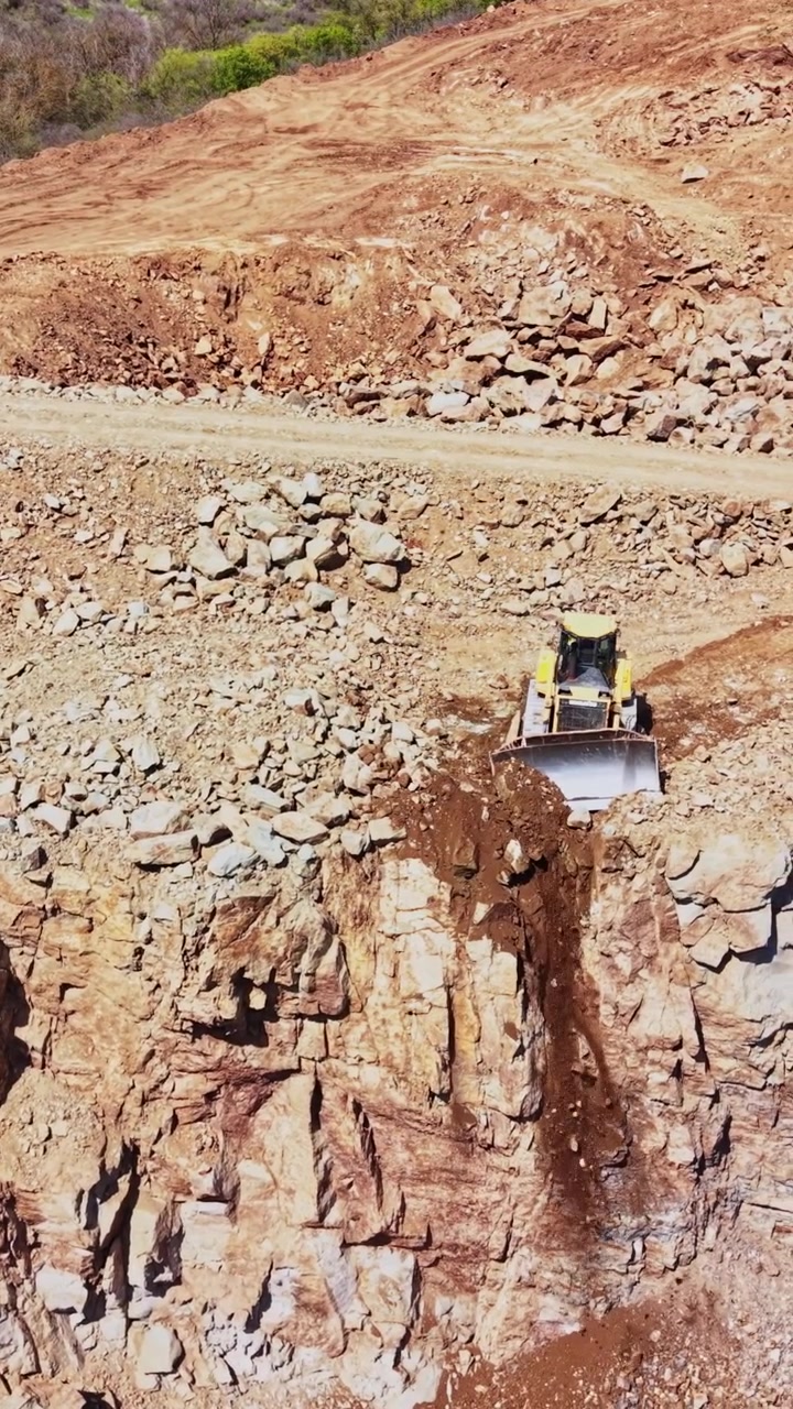 Canteiro de obras com máquinas pesadas trabalhando em terreno rochoso.